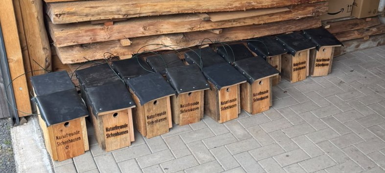 Hölzerne Nistkästen mit dem Namen Naturfreunde Sichenhausen vor einer Holzwand